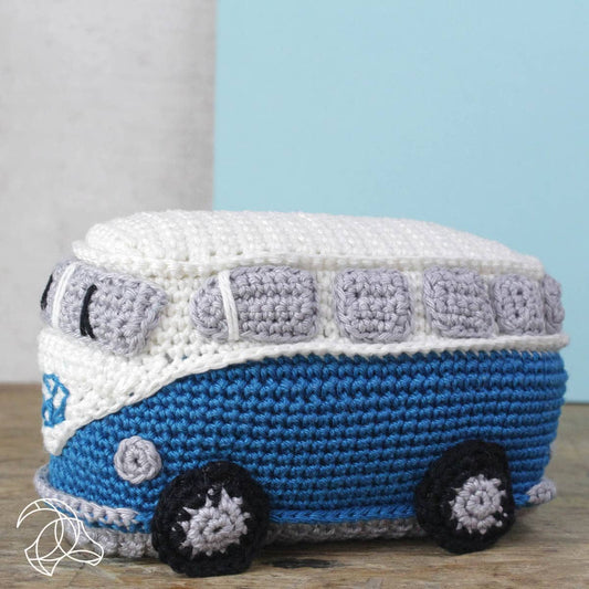 Crocheted blue and white van toy on a wooden surface with a light blue wall in the background.