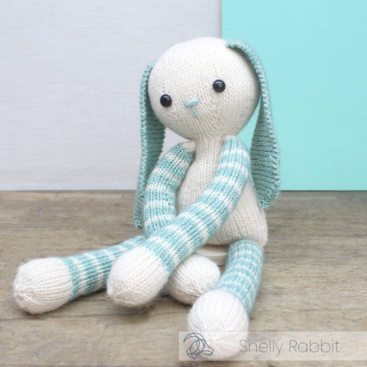 Knitted toy rabbit with striped arms and legs on a wooden surface