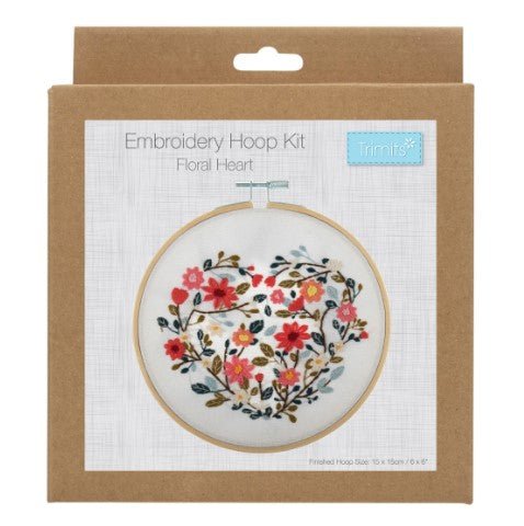 Packaged embroidery hoop kit with floral heart design on fabric, bamboo hoop, and embroidery threads visible through the packaging.
