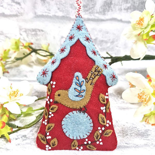 A felt craft kit depicting a Scandinavian-style embroidered birdhouse with a red roof, blue base, and a bird design in the center, surrounded by floral patterns.
