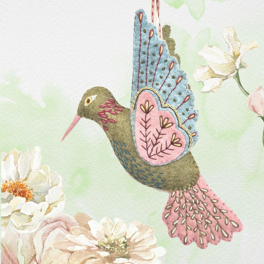 Decorative hummingbird ornament with floral patterns on a soft green background with flowers.