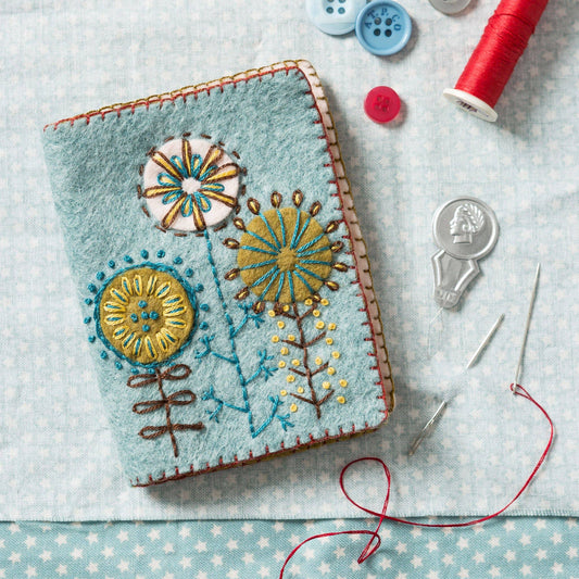 Embroidered notebook with floral designs on a tablecloth with sewing supplies.