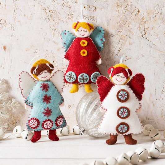 Three felt angel ornaments with colorful dresses on a textured surface.